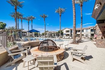A fire pit with chairs around it near a pool with palm trees